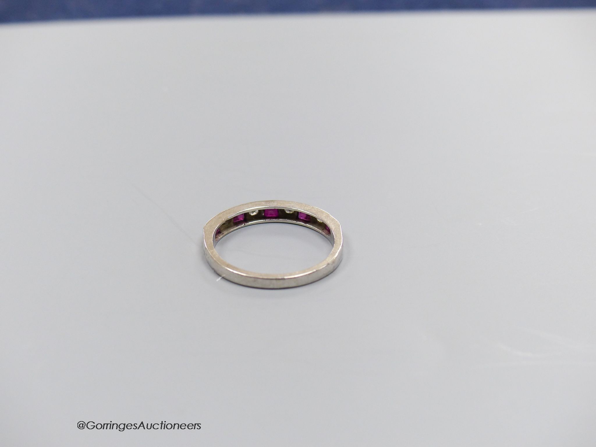 And 18 carat white gold ruby and diamond half eternity ring, size O, gross 2.7g.